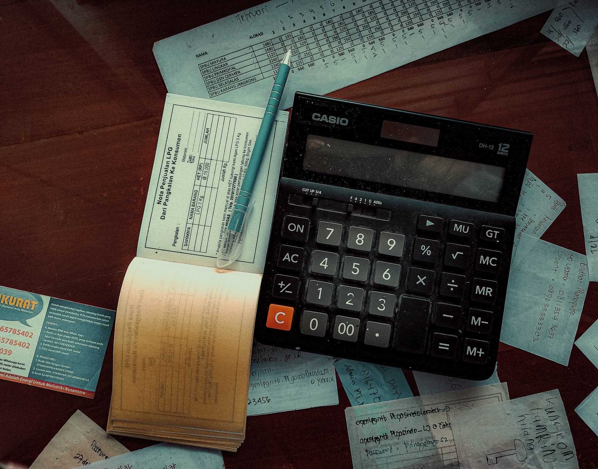 Un birou văzut de sus, acoperit cu însemnări de mână, chitanțiere cu indigo și un calculator de birou mare.
